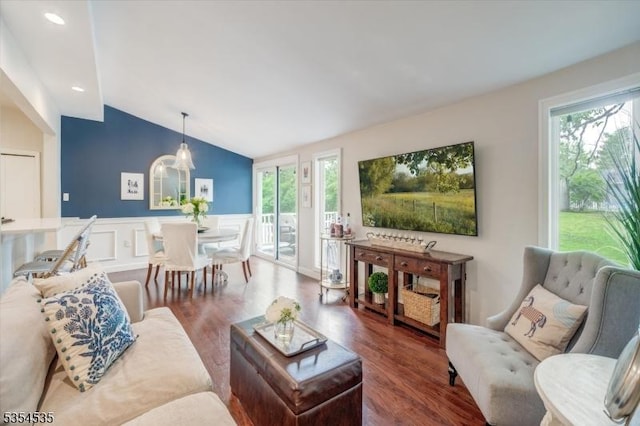 living area featuring wood finished floors, vaulted ceiling, plenty of natural light, wainscoting, and a decorative wall
