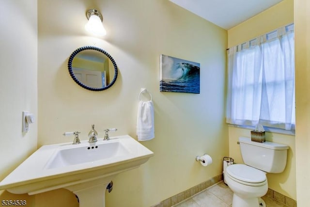 half bath with baseboards, a sink, tile patterned floors, and toilet