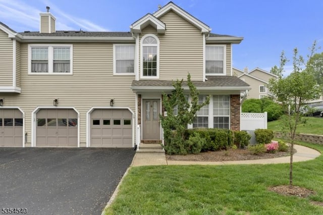 view of front of home featuring a garage, asphalt driveway, a chimney, and a front lawn