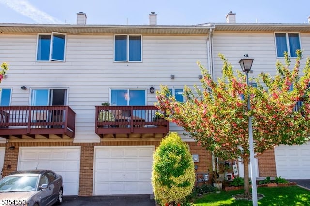 back of house with brick siding, driveway, a balcony, and a garage