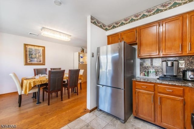 kitchen with visible vents, freestanding refrigerator, decorative backsplash, and brown cabinets