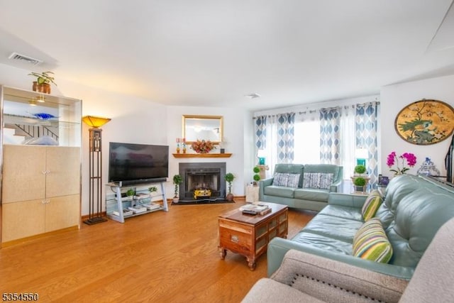 living room featuring visible vents, a fireplace with flush hearth, and wood finished floors