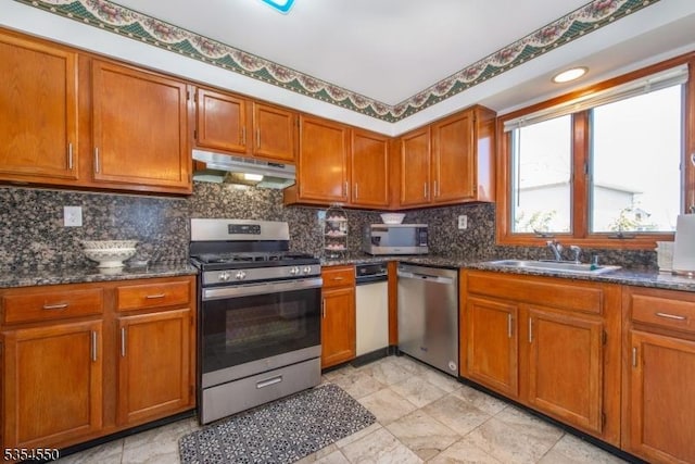 kitchen featuring brown cabinetry, tasteful backsplash, a sink, under cabinet range hood, and stainless steel appliances