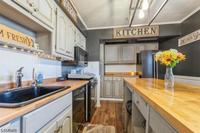 kitchen featuring wooden counters, crown molding, dark wood finished floors, a sink, and black appliances