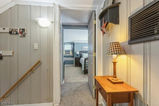 hall with ornamental molding, a decorative wall, and light colored carpet