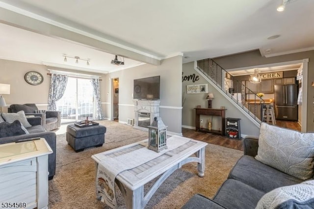 living room with track lighting, crown molding, wood finished floors, a fireplace, and stairway