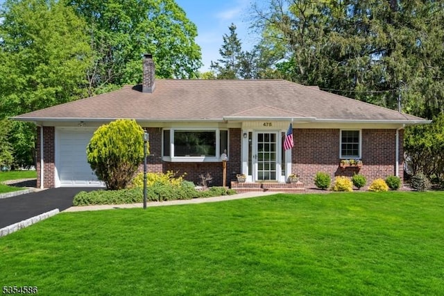 ranch-style house with a chimney, an attached garage, a front yard, and brick siding
