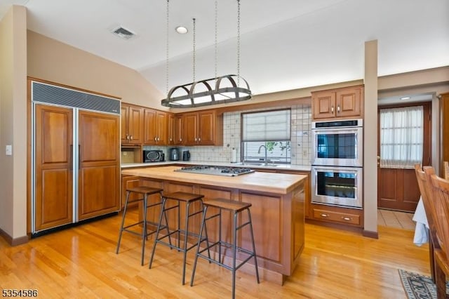 kitchen with paneled built in fridge, double oven, gas stovetop, light wood-type flooring, and visible vents