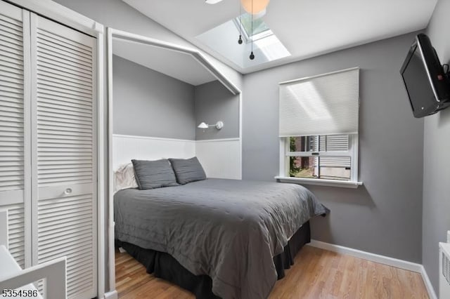 bedroom featuring baseboards, wood finished floors, vaulted ceiling with skylight, and a closet