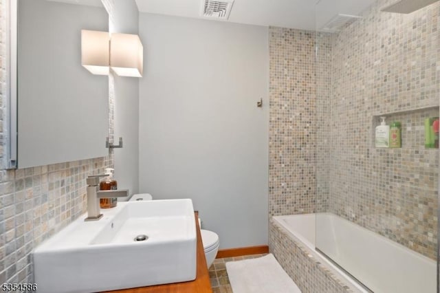 bathroom with tile patterned flooring, toilet, tiled shower / bath, tile walls, and visible vents
