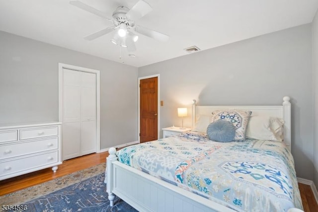 bedroom featuring a ceiling fan, visible vents, wood finished floors, baseboards, and a closet