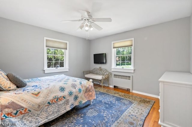 bedroom with wood finished floors, baseboards, radiator heating unit, and multiple windows