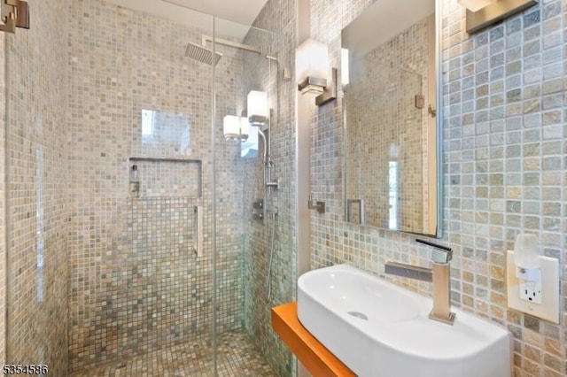 full bathroom with a sink, a shower stall, tasteful backsplash, and tile walls