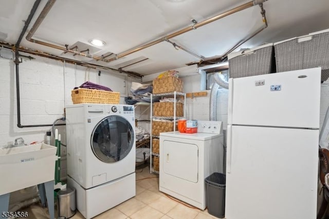 washroom with laundry area, a sink, separate washer and dryer, concrete block wall, and light tile patterned floors