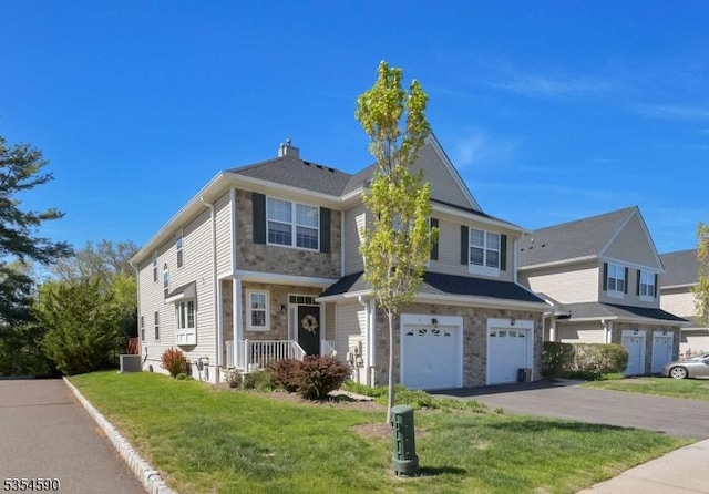 traditional home with driveway, a chimney, a front lawn, an attached garage, and stone siding