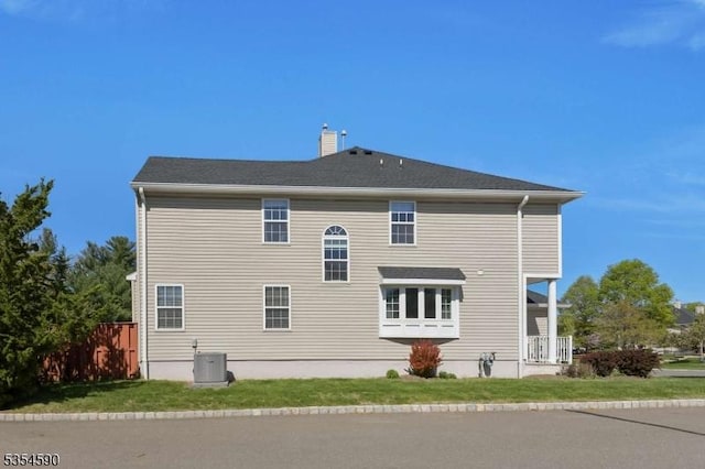 rear view of property featuring central air condition unit, a yard, a chimney, and fence