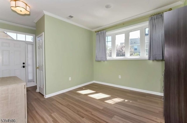 spare room with crown molding, baseboards, wood finished floors, and visible vents
