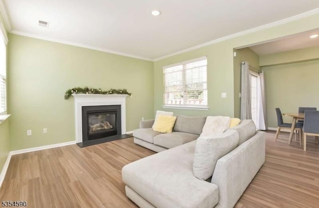 living room featuring crown molding, baseboards, light wood finished floors, and visible vents