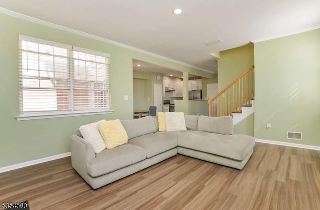 living area featuring baseboards, visible vents, ornamental molding, and wood finished floors
