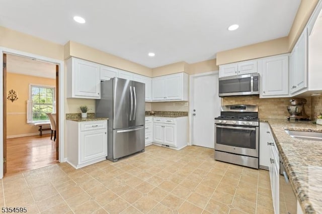 kitchen featuring stainless steel appliances, light stone counters, and white cabinetry