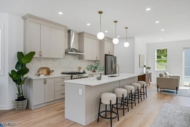 kitchen with wall chimney range hood, freestanding refrigerator, light wood finished floors, decorative backsplash, and recessed lighting