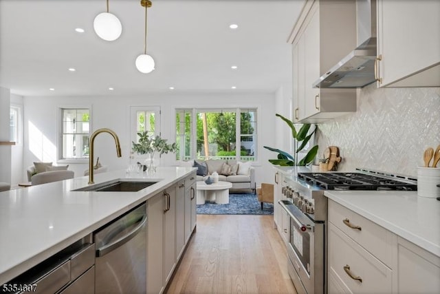 kitchen featuring appliances with stainless steel finishes, a sink, open floor plan, wall chimney exhaust hood, and light countertops