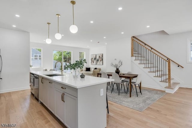 kitchen featuring a sink, light wood finished floors, light countertops, an island with sink, and hanging light fixtures