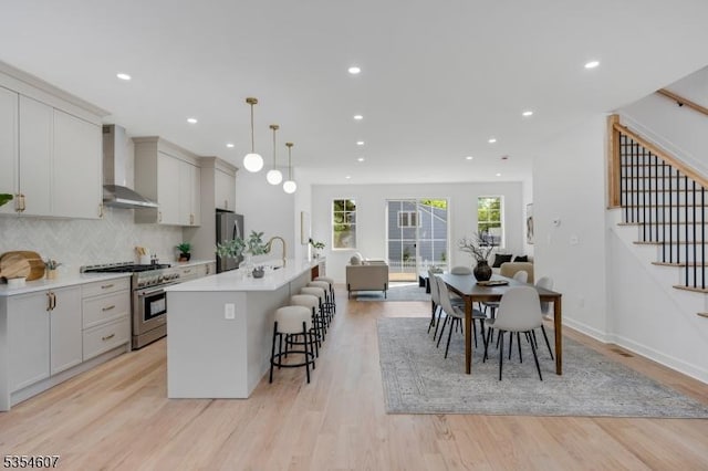 kitchen featuring stainless steel appliances, wall chimney range hood, a kitchen bar, light countertops, and recessed lighting