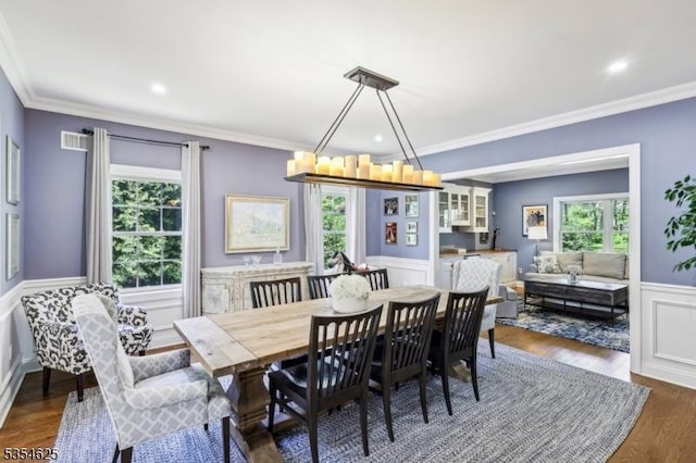 dining space with crown molding, dark wood-style flooring, a decorative wall, a wainscoted wall, and visible vents