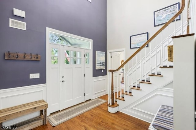 foyer with stairway, a high ceiling, wood finished floors, and visible vents