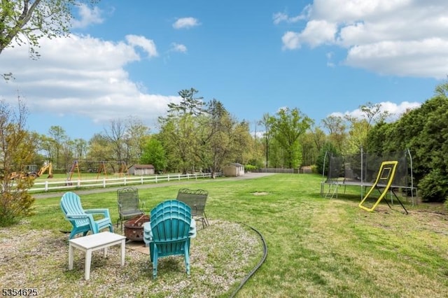 view of yard with a fenced backyard, an outbuilding, a trampoline, an outdoor fire pit, and a storage shed