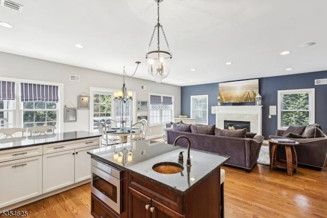 kitchen featuring visible vents, stainless steel microwave, a chandelier, a sink, and light wood-style flooring