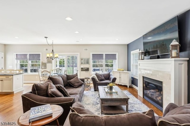living area with visible vents, recessed lighting, a high end fireplace, light wood finished floors, and a notable chandelier