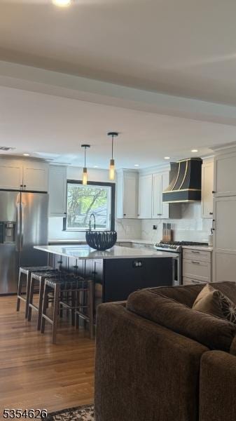 kitchen with pendant lighting, wood finished floors, open floor plan, wall chimney exhaust hood, and appliances with stainless steel finishes
