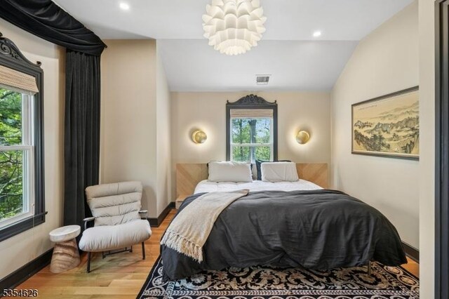 bedroom featuring visible vents, light wood-style flooring, vaulted ceiling, and multiple windows