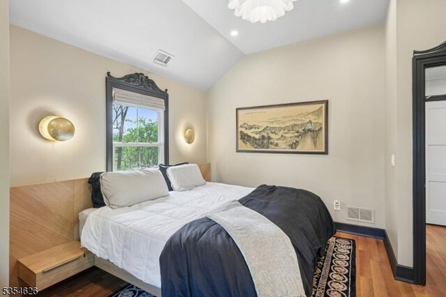 bedroom with a notable chandelier, lofted ceiling, wood finished floors, and visible vents