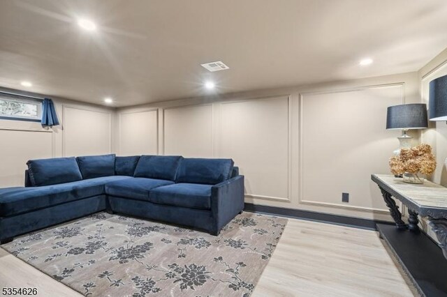 living room with recessed lighting, visible vents, wood finished floors, and a decorative wall