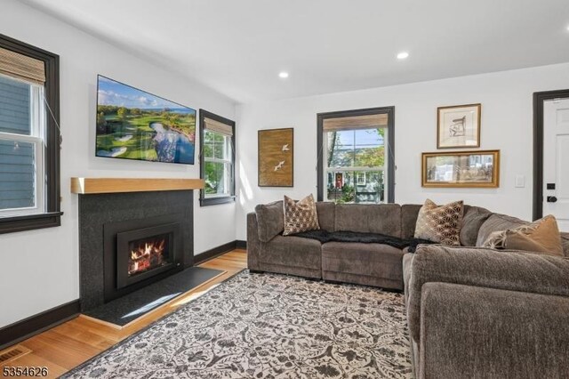 living room with a lit fireplace, visible vents, a wealth of natural light, and wood finished floors