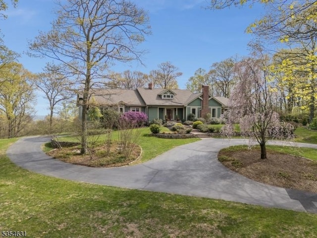 cape cod home with curved driveway, a front lawn, and a chimney