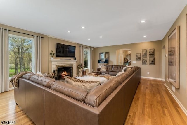 living area with arched walkways, baseboards, a warm lit fireplace, and light wood-style flooring