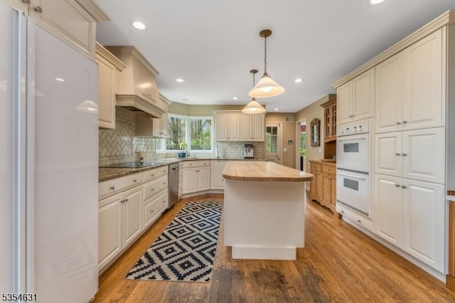 kitchen featuring hanging light fixtures, white appliances, light wood-style flooring, a center island, and decorative backsplash