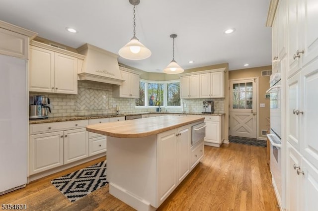 kitchen featuring a kitchen island, premium range hood, built in fridge, tasteful backsplash, and hanging light fixtures