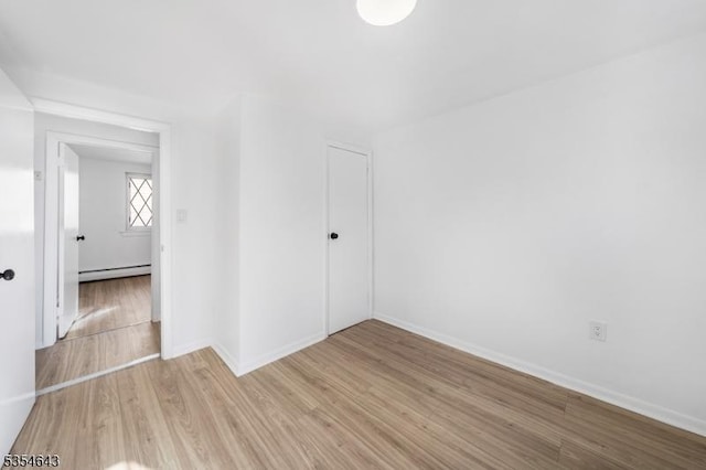 unfurnished room with baseboard heating, baseboards, and wood finished floors