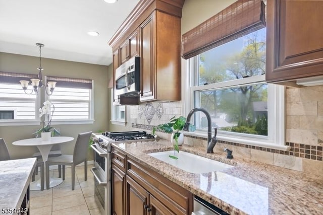 kitchen featuring appliances with stainless steel finishes, brown cabinets, a sink, light stone counters, and a chandelier