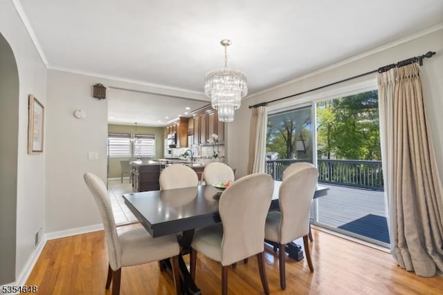 dining space with crown molding, baseboards, a chandelier, arched walkways, and light wood finished floors
