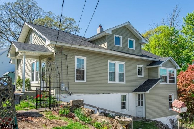rear view of property featuring a shingled roof and a chimney