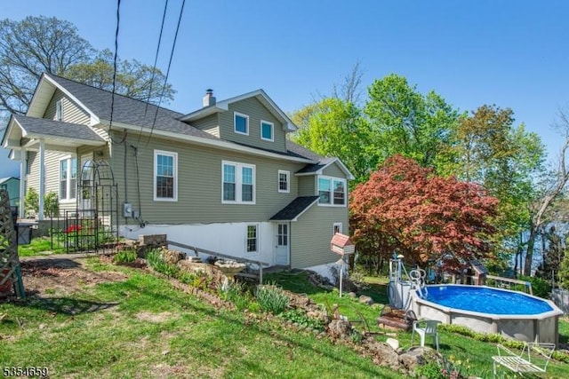 rear view of property featuring a shingled roof and an outdoor pool