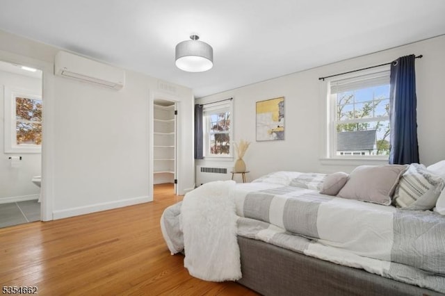 bedroom with a closet, a wall mounted air conditioner, radiator heating unit, a spacious closet, and light wood-style flooring