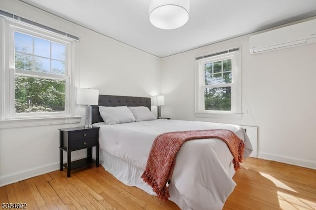 bedroom with baseboards, a wall unit AC, and wood finished floors
