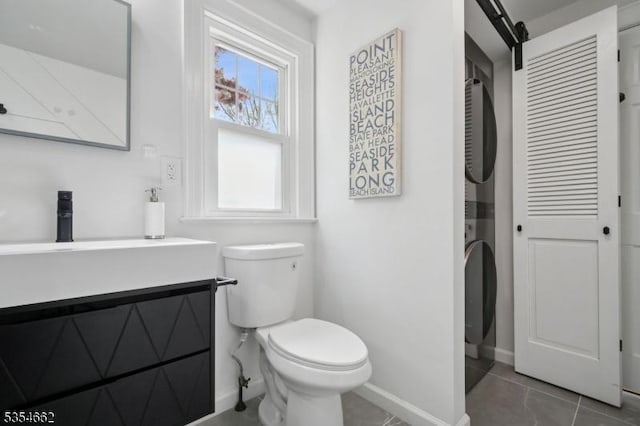 bathroom featuring tile patterned floors, baseboards, vanity, toilet, and stacked washer and clothes dryer
